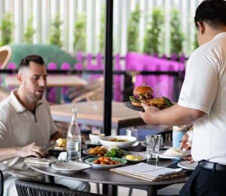 Server bringing a burger and sharing plates to a guest's table