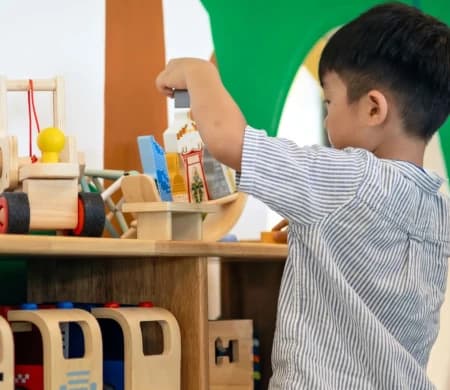 Boy choosing wooden toys from the play shelf at Flying Lizard