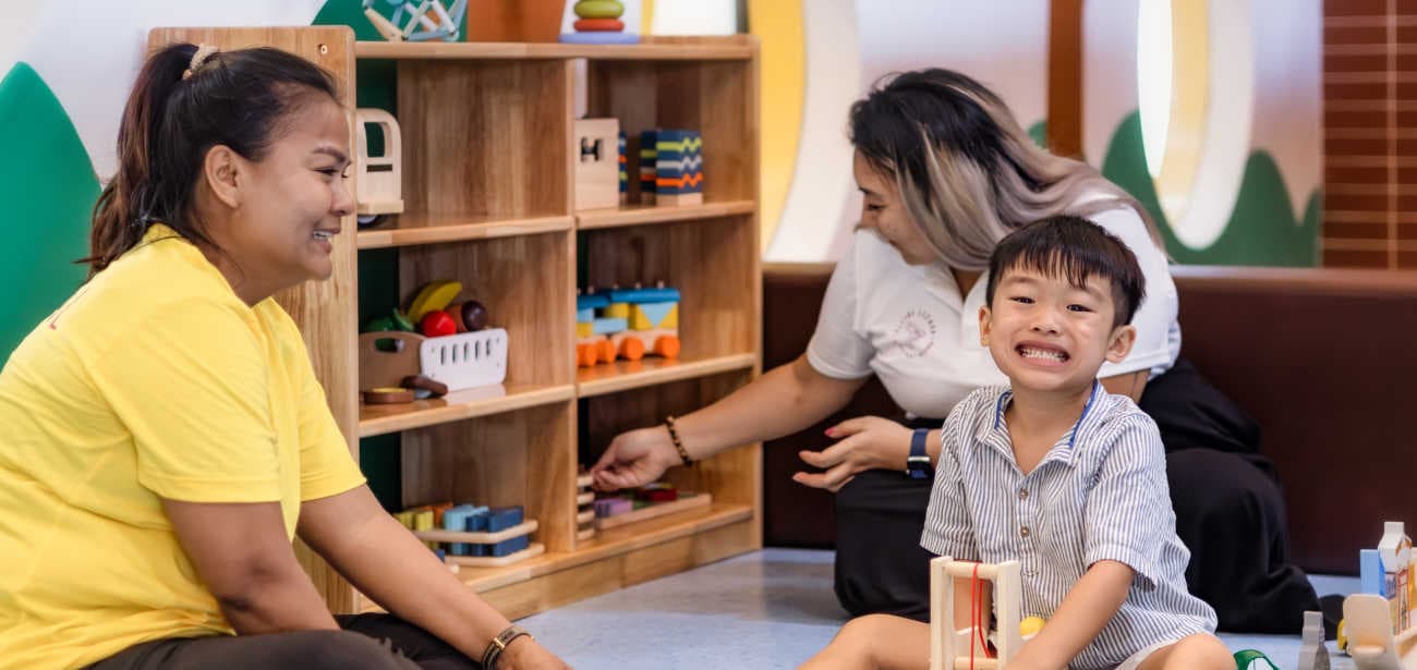 Child playing with wooden toys alongside Flying Lizard kids club staff