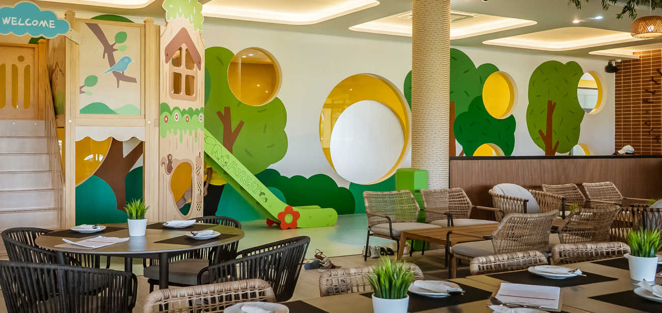 Forest-themed indoor play area with slide and treehouse beside the dining tables